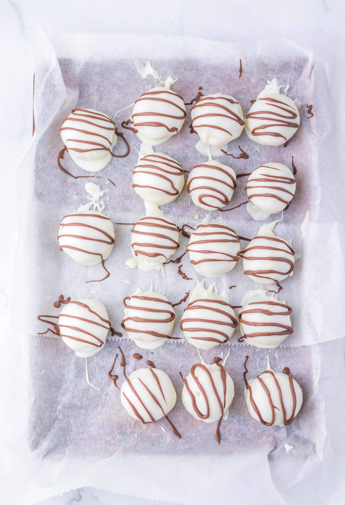 Sixteen Zebra Cake Balls, featuring white chocolate truffles with milk chocolate drizzle, are artfully arranged on parchment paper.