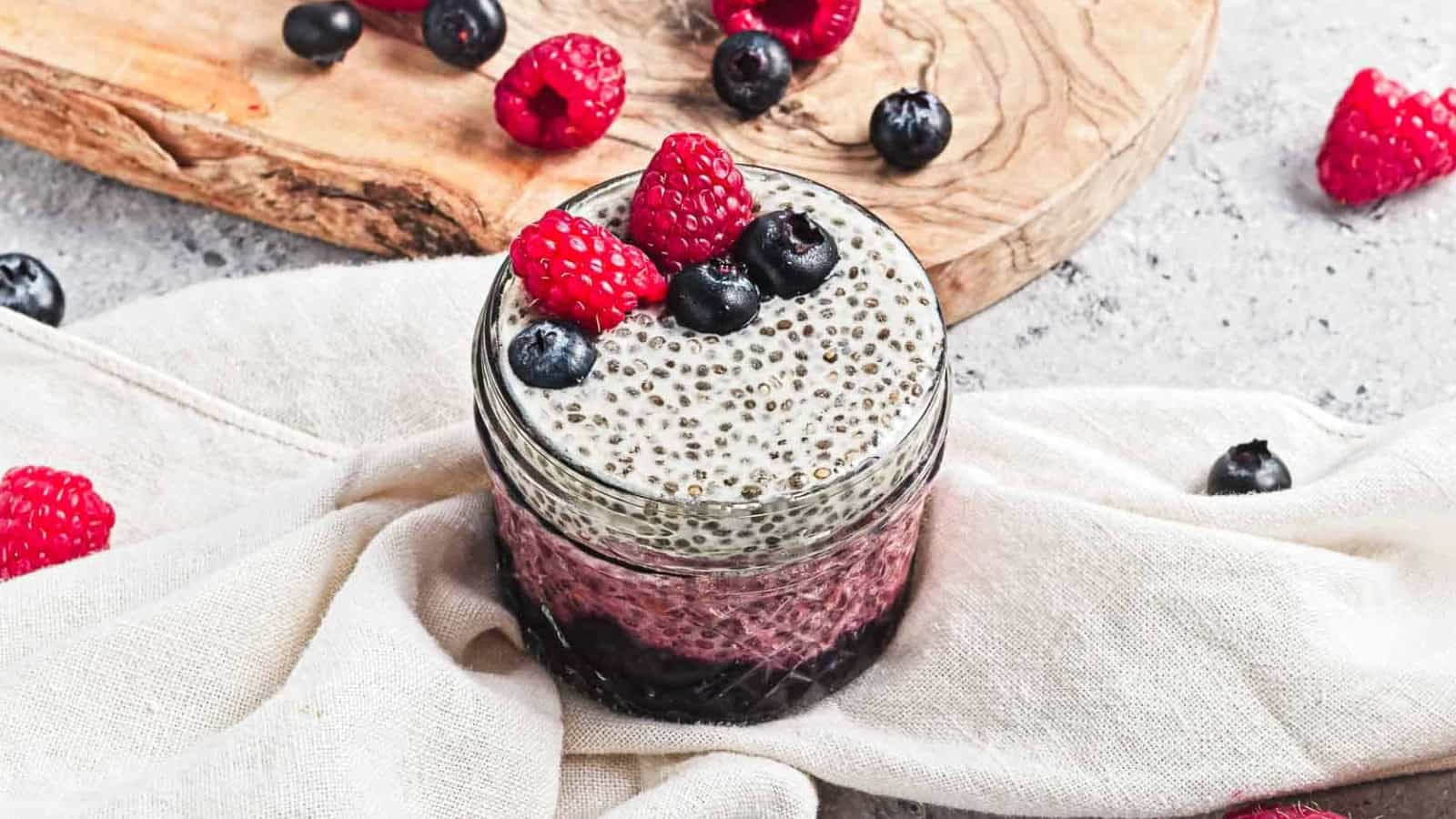 Layered chia pudding in jars topped with raspberries and blueberries, surrounded by scattered berries.