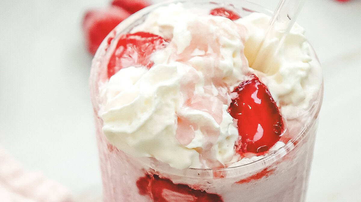 A close-up of a Strawberry Cheesecake Frappuccino copycat recipe, topped with whipped cream and strawberry pieces in a clear glass, just like your favorite Starbucks treat.