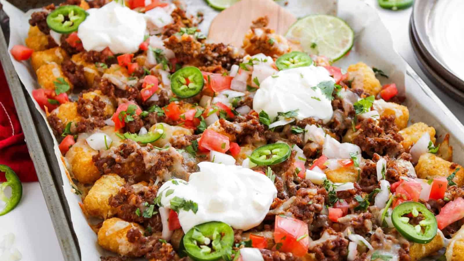 Tater tots topped with ground beef, cheese, tomatoes, onions, jalapeรฑos, and dollops of sour cream.