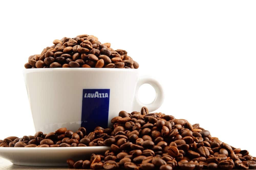 A white Lavazza cup filled with coffee beans, surrounded by more coffee beans on a white background, showcases the essence of the best ground coffee.