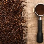 Coffee beans on burlap next to a portafilter filled with the best ground coffee, shot from above.