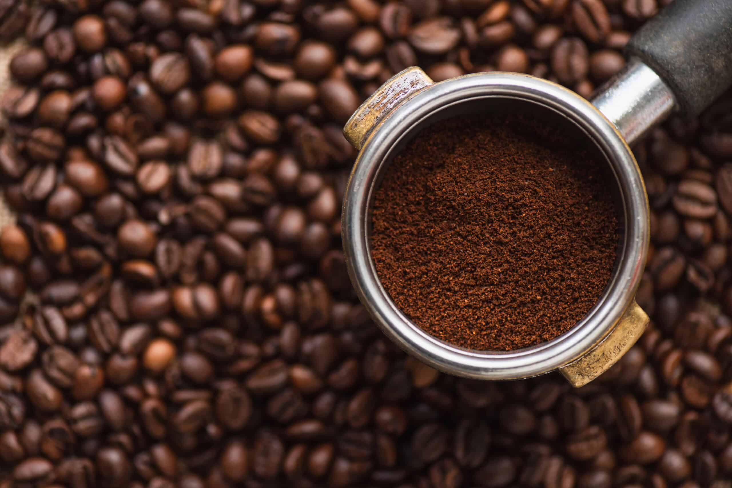 Portafilter with the best ground coffee on top of a pile of whole coffee beans, viewed from above.