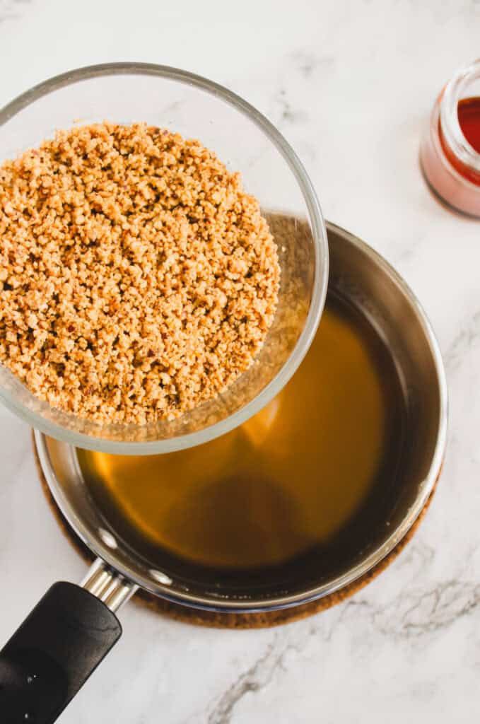 A bowl of ground nuts held over a saucepan of melted butter on a marble countertop, perfect for creating your own rich hazelnut syrup recipe.