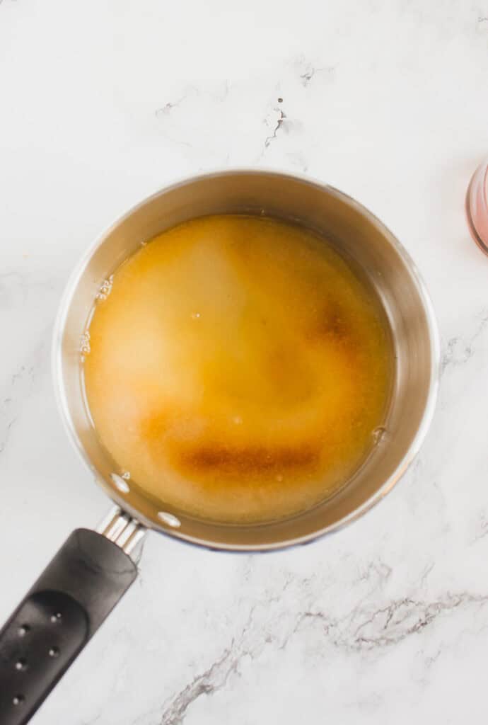 A saucepan with a light brown homemade hazelnut syrup mixture on a white marble surface, viewed from above.
