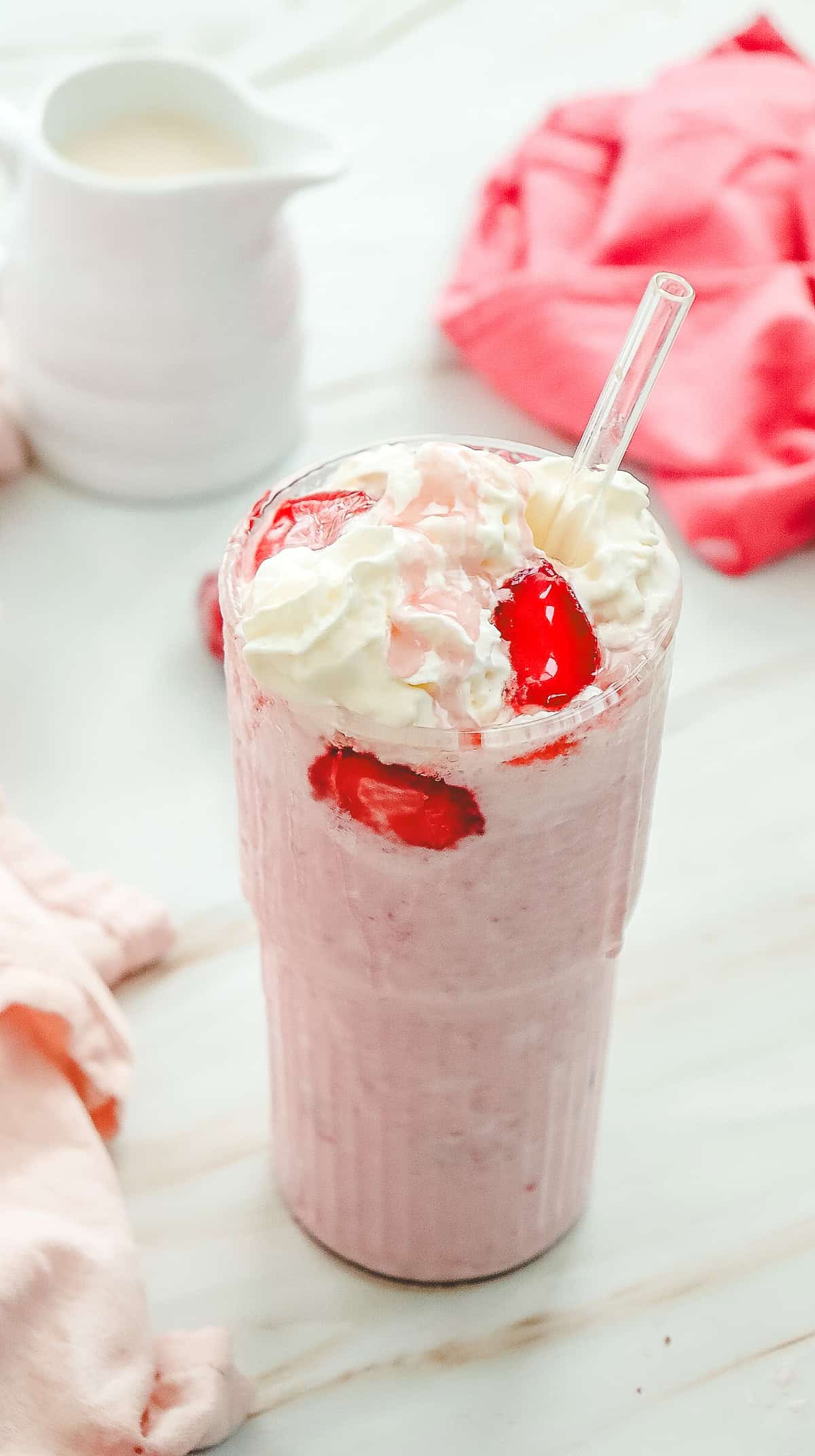 A strawberry milkshake topped with whipped cream and strawberry slices in a tall glass with a straw, inspired by the popular Starbucks Copycat Strawberry Cheesecake Frappucino recipe.