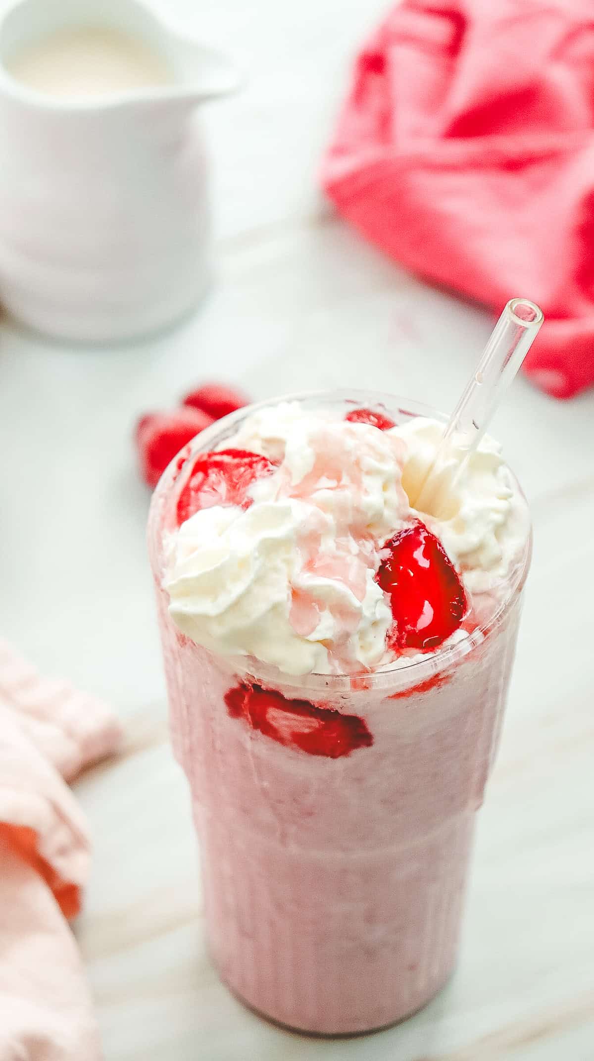 A Strawberry Cheesecake Frappucino topped with whipped cream, strawberry slices, and a clear straw on a light surface&mdash;perfect for those craving a Starbucks copycat treat.