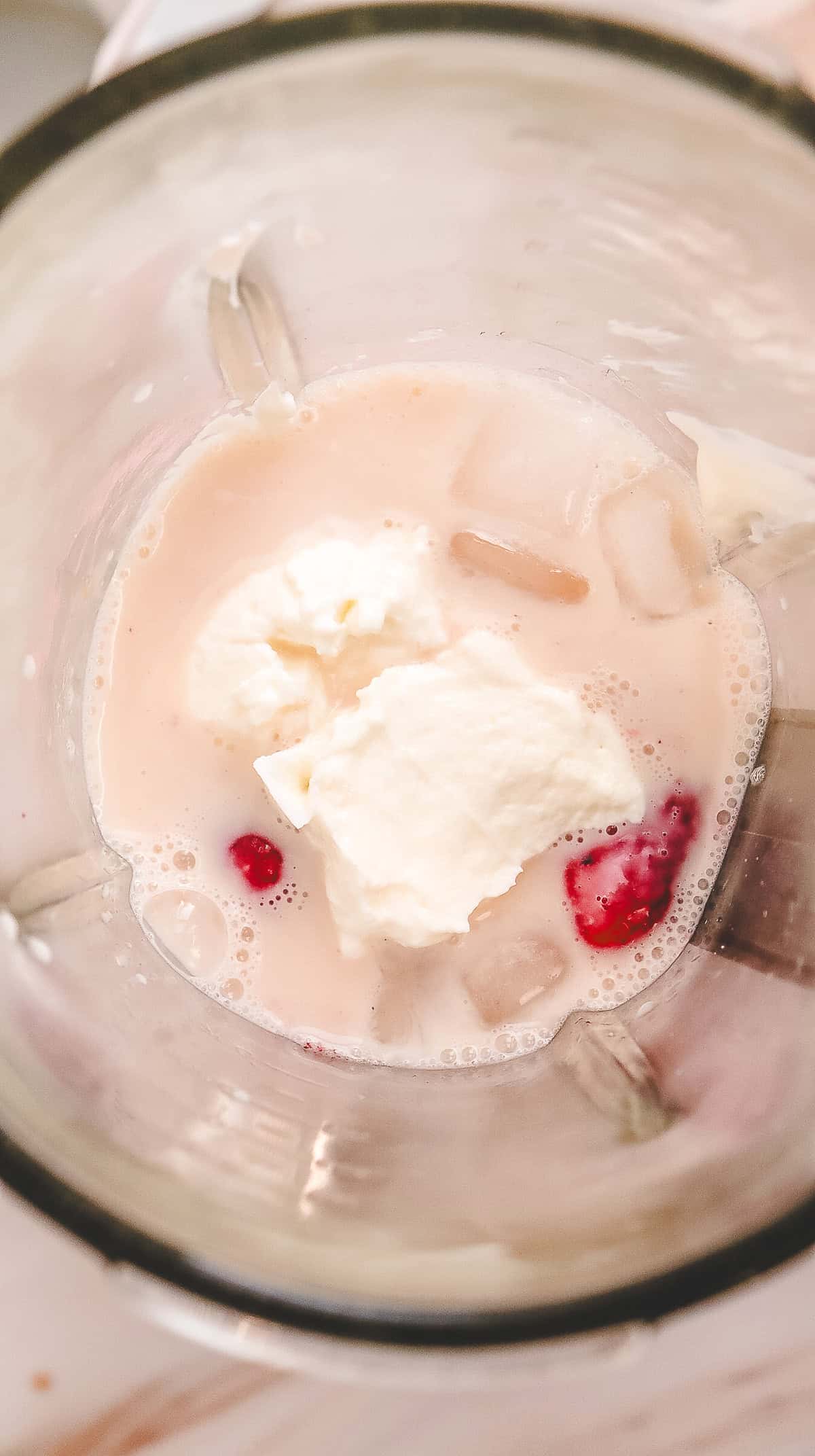 Milk, ice, whipped cream, and a few strawberries in a blender, viewed from above&mdash;ready to blend into a delicious Strawberry Cheesecake Frappuccino Starbucks Copycat recipe.