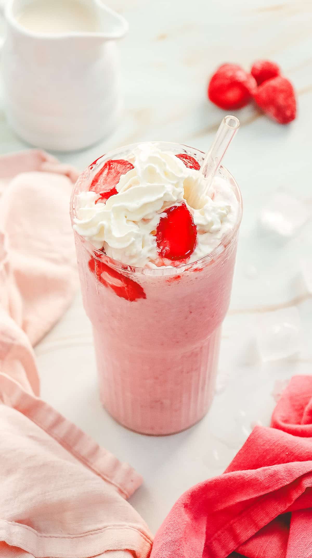 A pink strawberry milkshake inspired by a Starbucks Copycat Strawberry Cheesecake Frappuccino, topped with whipped cream and strawberries, served with a clear straw in a glass.