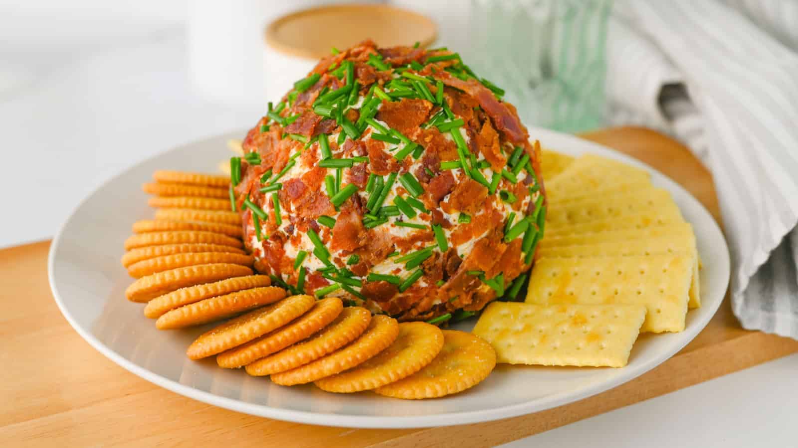 Cheese ball coated in nuts, surrounded by crackers, tomatoes, radishes, and cucumber slices on a platter.
