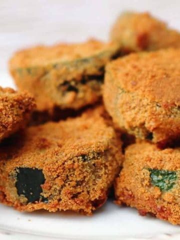 Golden, crispy breaded zucchini rounds stacked on a white plate, ready to eat.