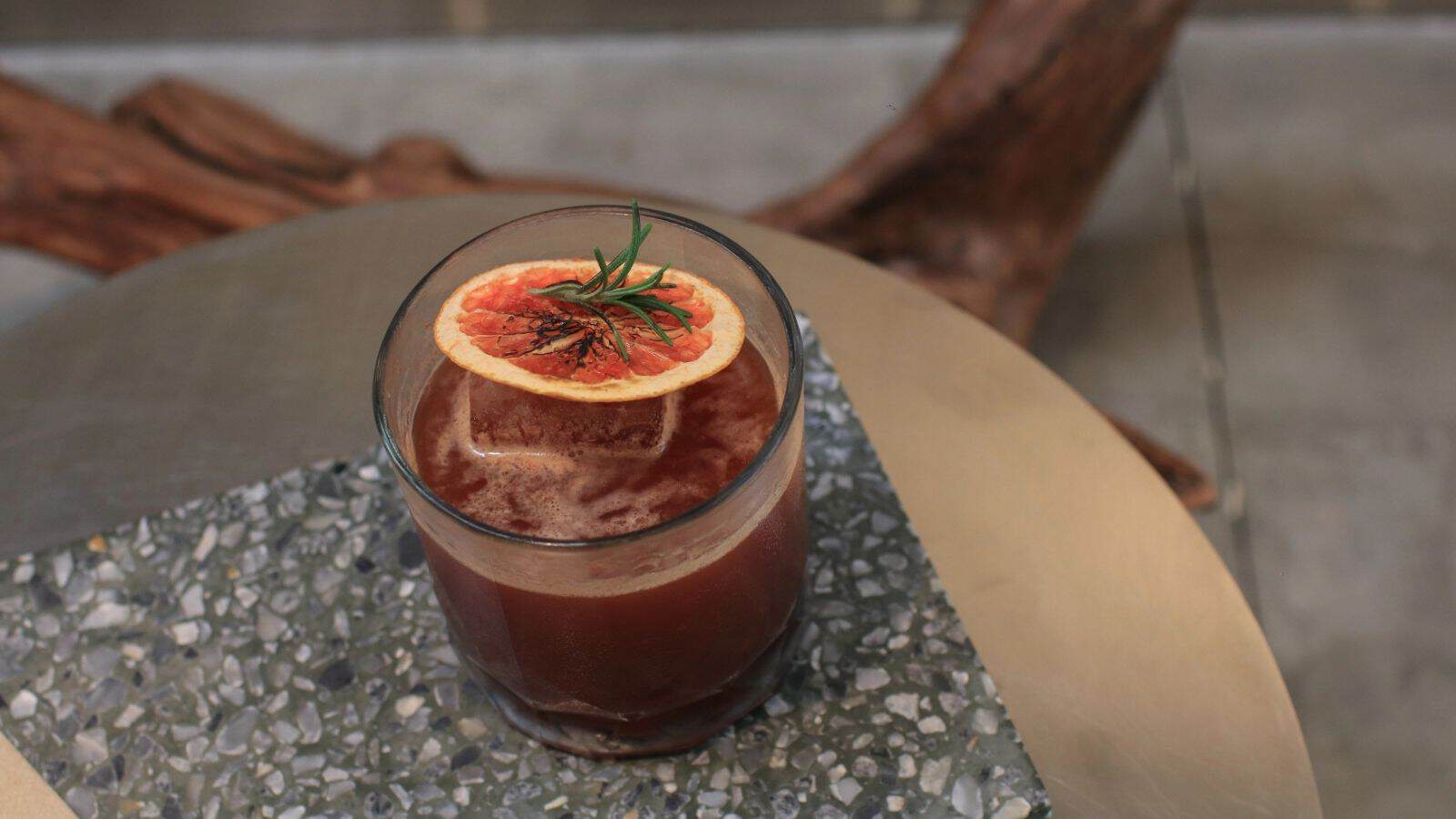 A dark mocktail garnished with a dried orange slice and rosemary, served on a terrazzo table&mdash;perfect for those seeking sophisticated non-alcoholic drinks.