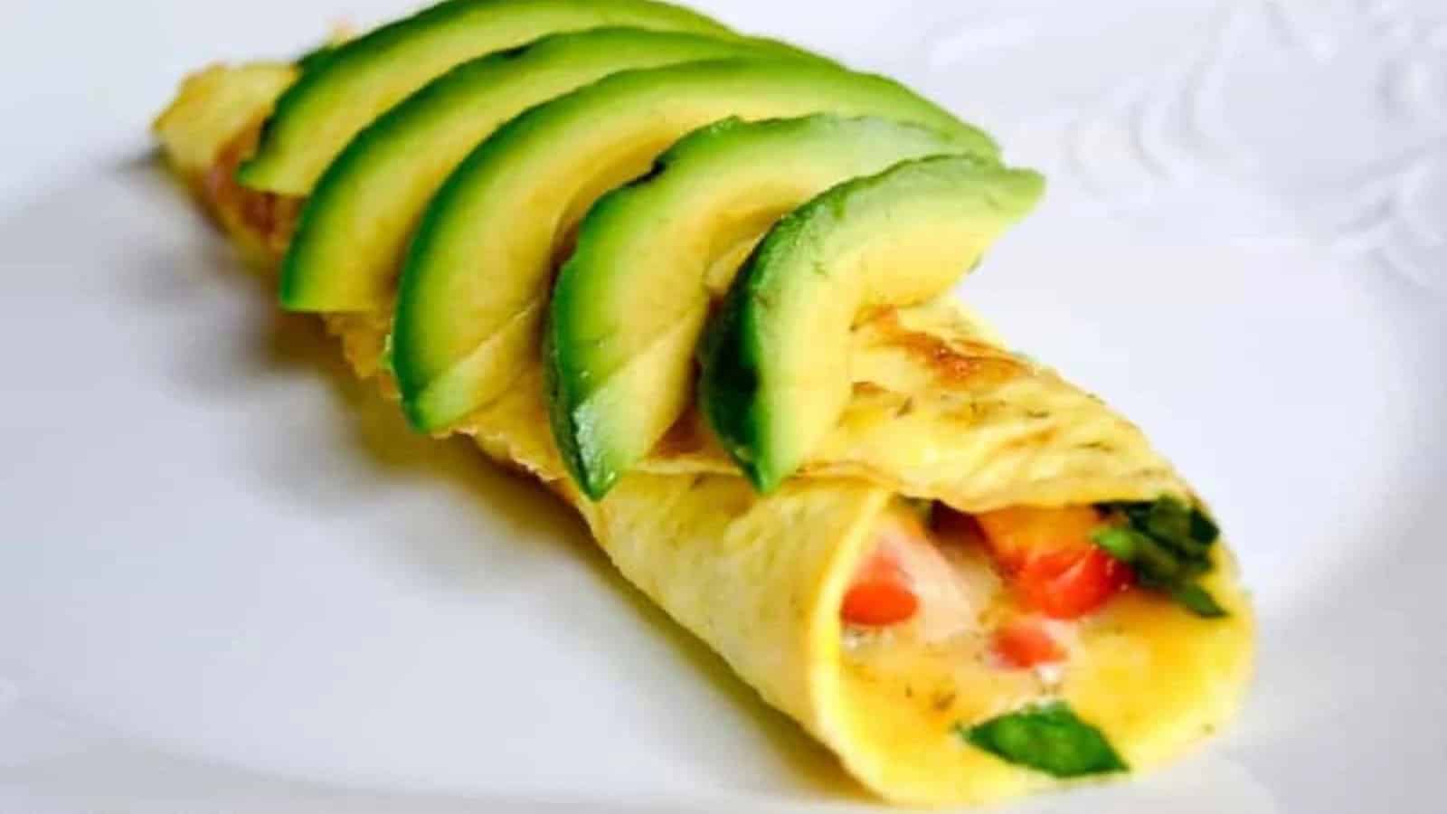 A veggie omelet on a white plate topped with fresh avocado.
