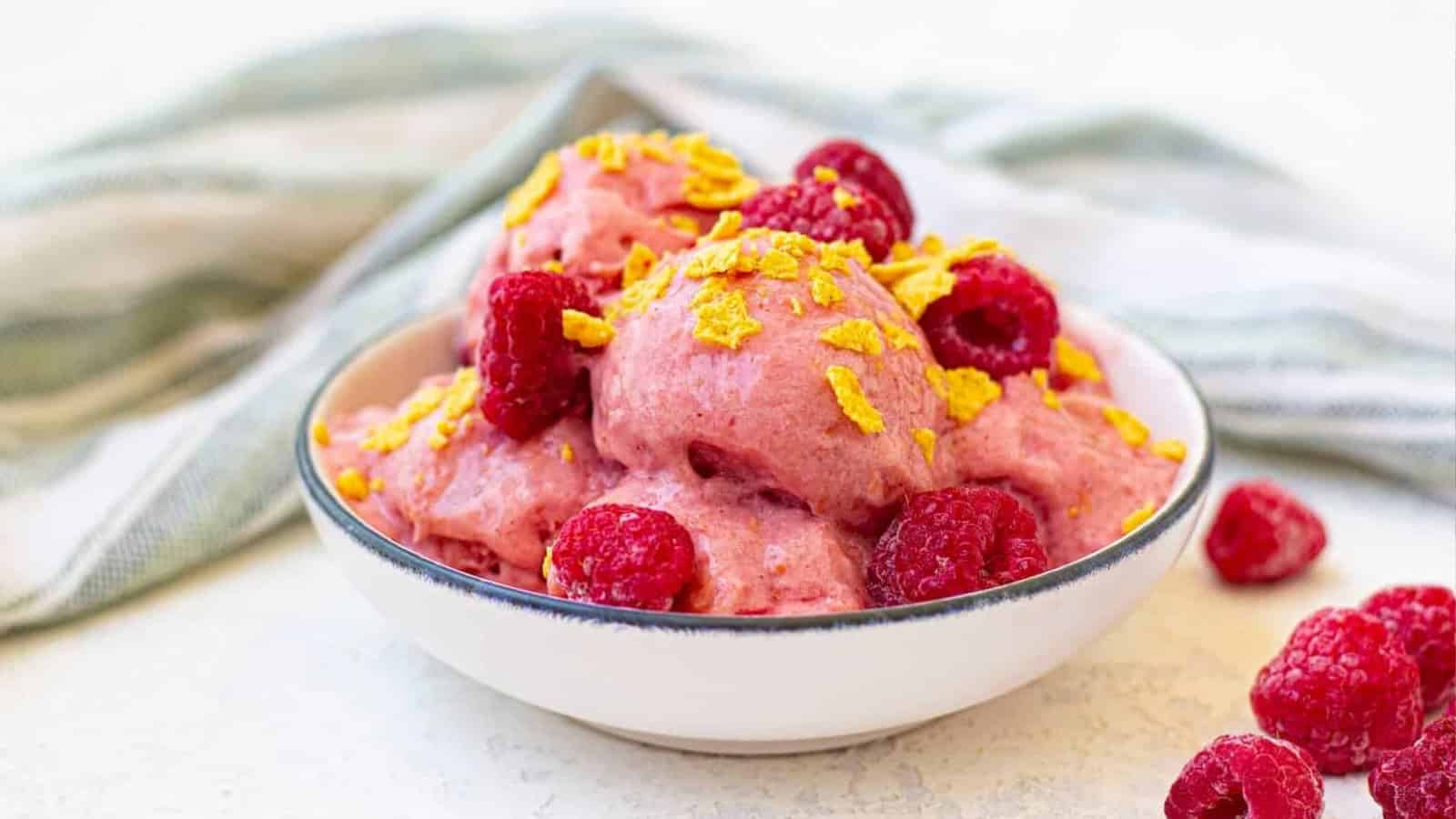 A bowl of frozen yogurt with raspberries and corn flakes.