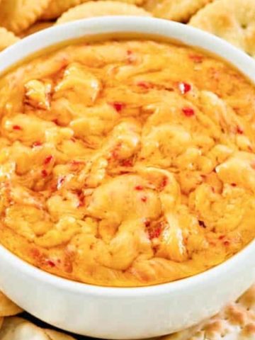 A bowl of pimento cheese dip surrounded by round crackers.