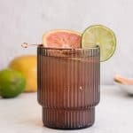 A brown ribbed glass filled with a refreshing Sparkling Grapefruit Mocktail, garnished with a lime and grapefruit slice on a stick.