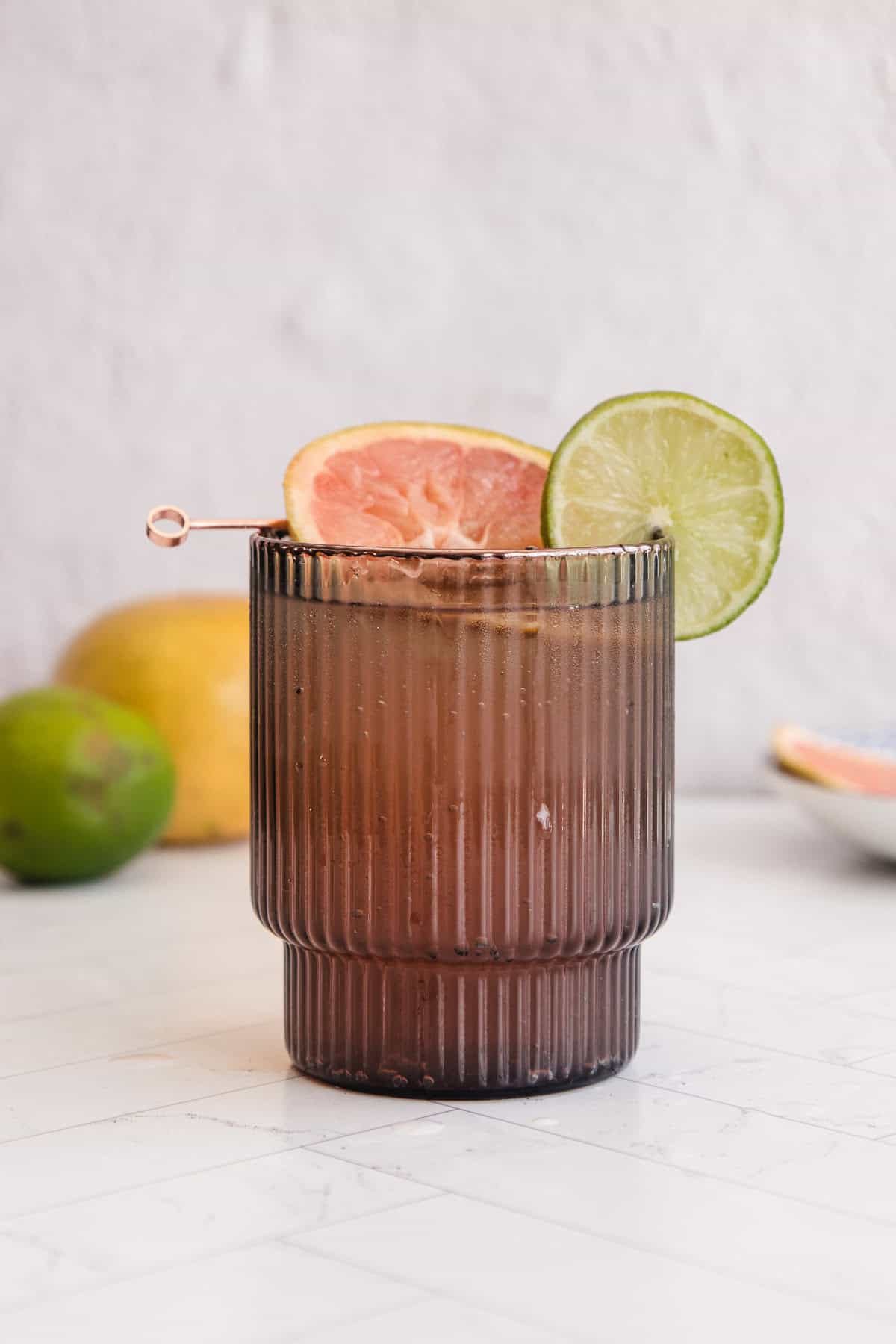 A brown ribbed glass filled with a refreshing Sparkling Grapefruit Mocktail, garnished with a lime and grapefruit slice on a stick.