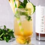 A tropical pineapple mojito mocktail garnished with pineapple, lime, mint, and a striped straw, served in a ribbed glass on a coaster.