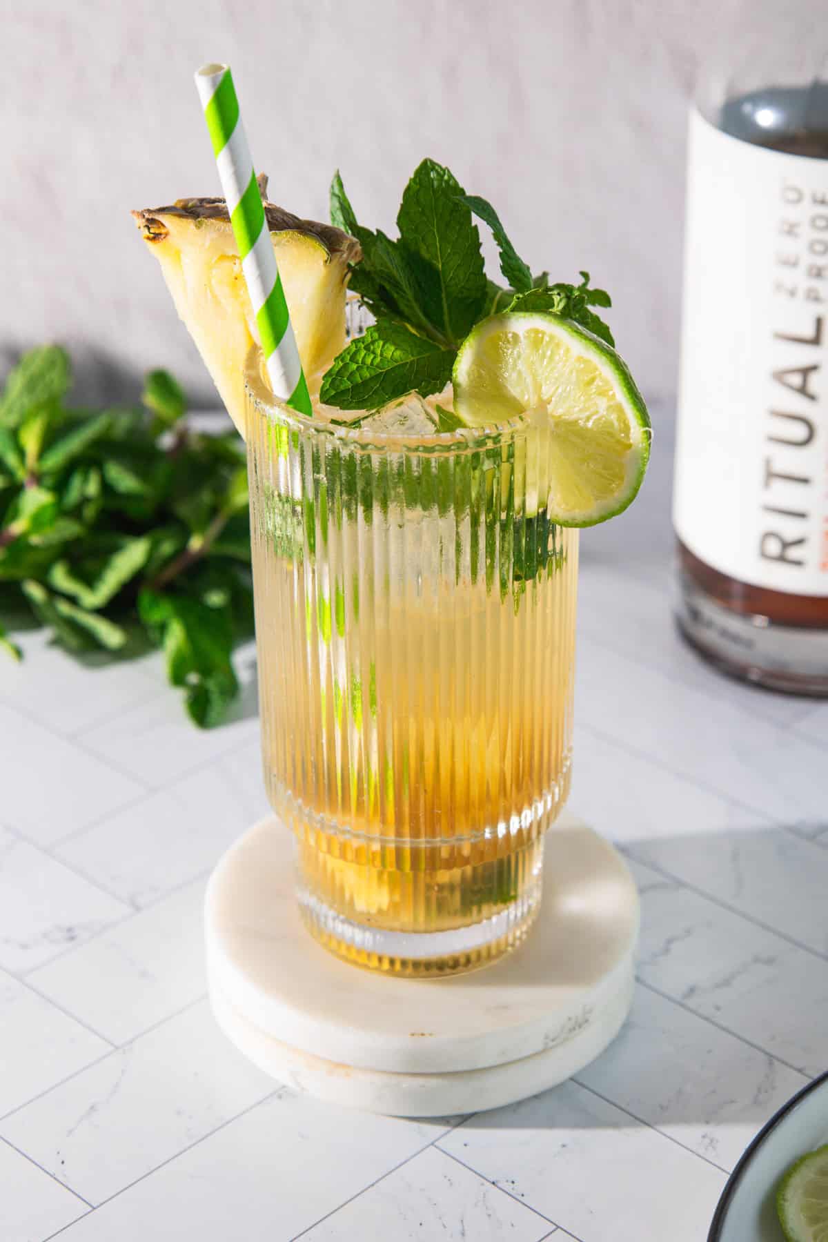 A refreshing pineapple mojito mocktail garnished with mint, lime, and pineapple, served with a green-striped straw on a marble coaster.