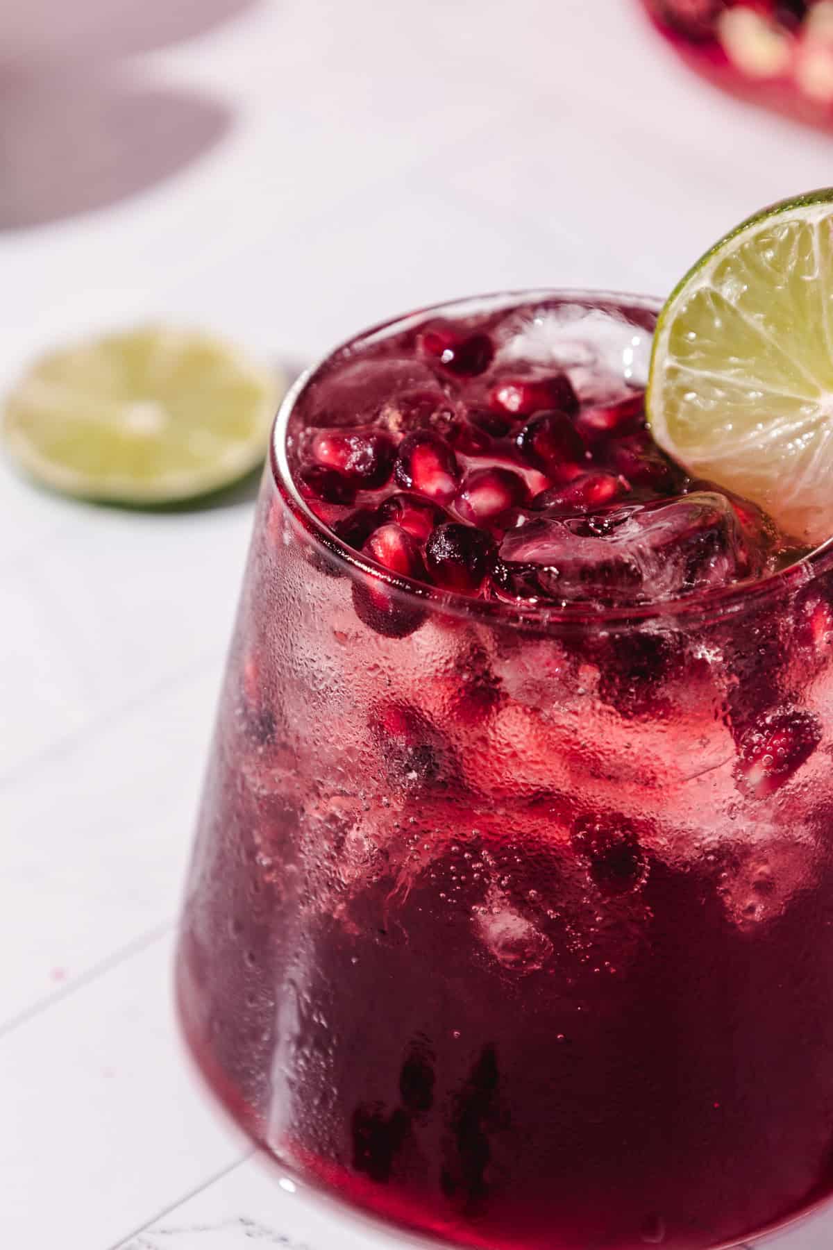 A refreshing pomegranate mocktail served in a glass with ice, pomegranate seeds, and a lime slice garnish.