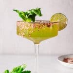 Green Spicy Margarita Mocktail in a glass with a salted rim, garnished with celery and a lime slice, on a light background.