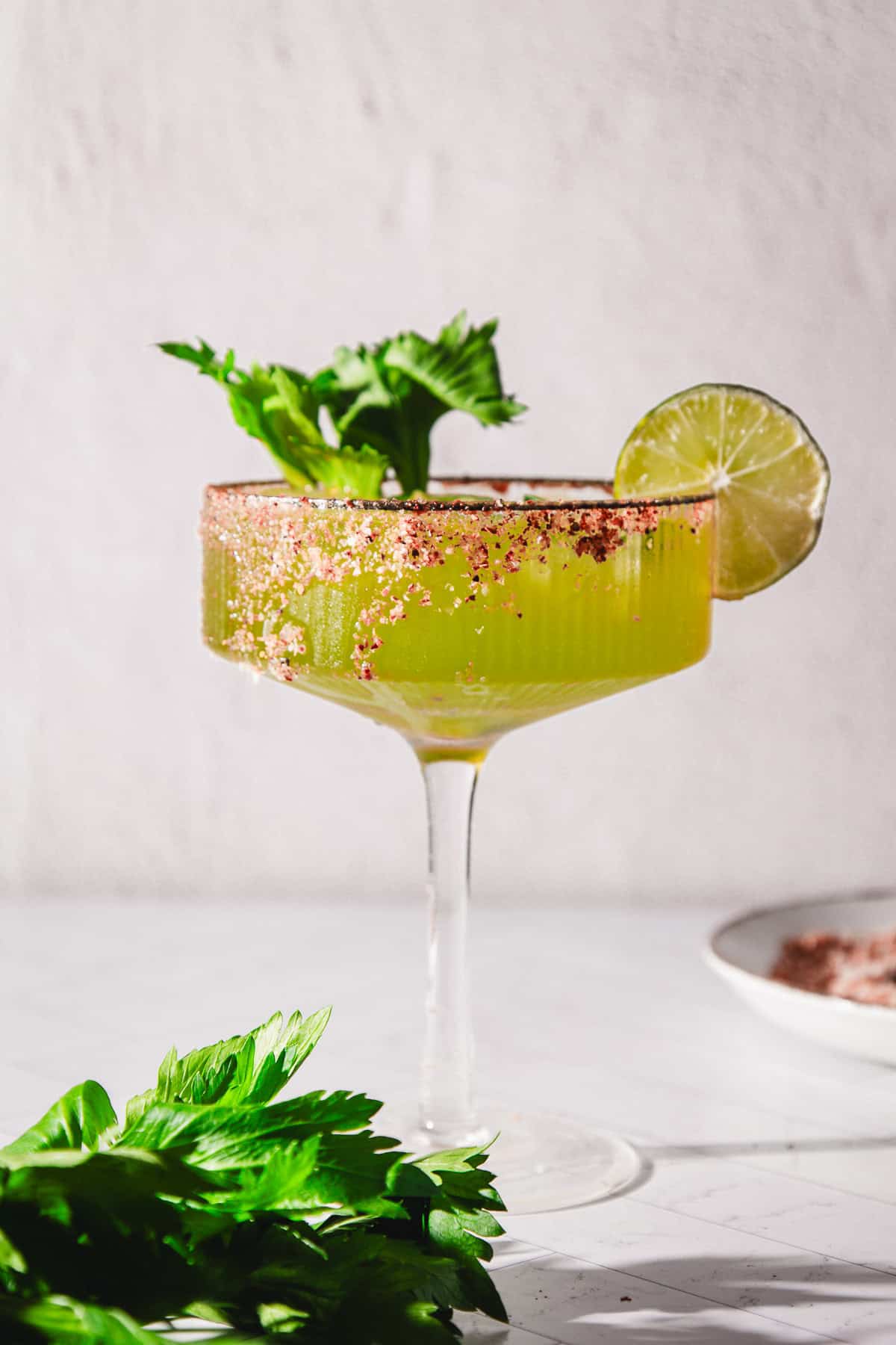 Green Spicy Margarita Mocktail in a glass with a salted rim, garnished with celery and a lime slice, on a light background.