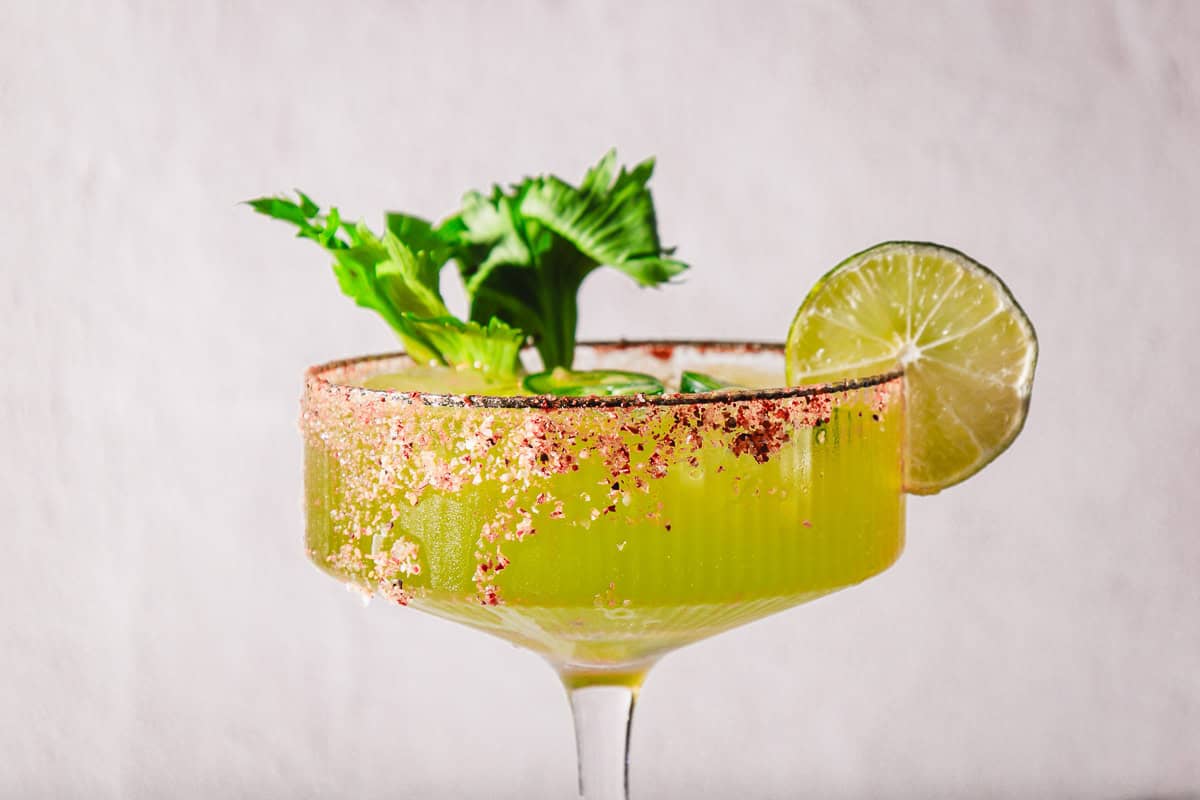 Spicy Margarita Mocktail served in a glass with a chili rim, lime slice, and green leafy garnish, set against a light background.