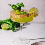 A green Spicy Margarita Mocktail in a glass with a spiced rim, garnished with a lime slice, celery, and jalapeño slices.