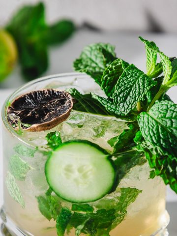 A virgin mint julep recipe comes to life in this cocktail, garnished with fresh mint, a cucumber slice, and a dried lime on a pristine white surface.
