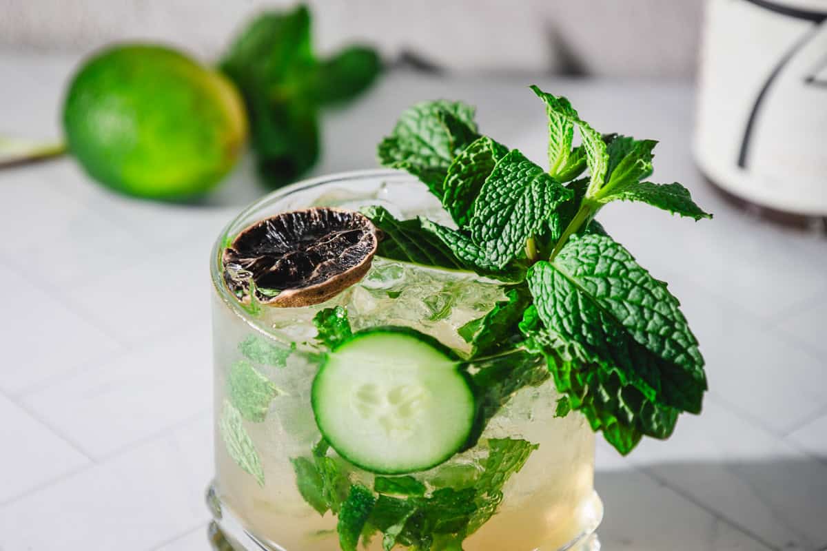 A virgin mint julep recipe comes to life in this cocktail, garnished with fresh mint, a cucumber slice, and a dried lime on a pristine white surface.