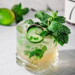 A virgin mint julep recipe comes to life in this cocktail, garnished with mint leaves and cucumber slices on a white tiled surface.