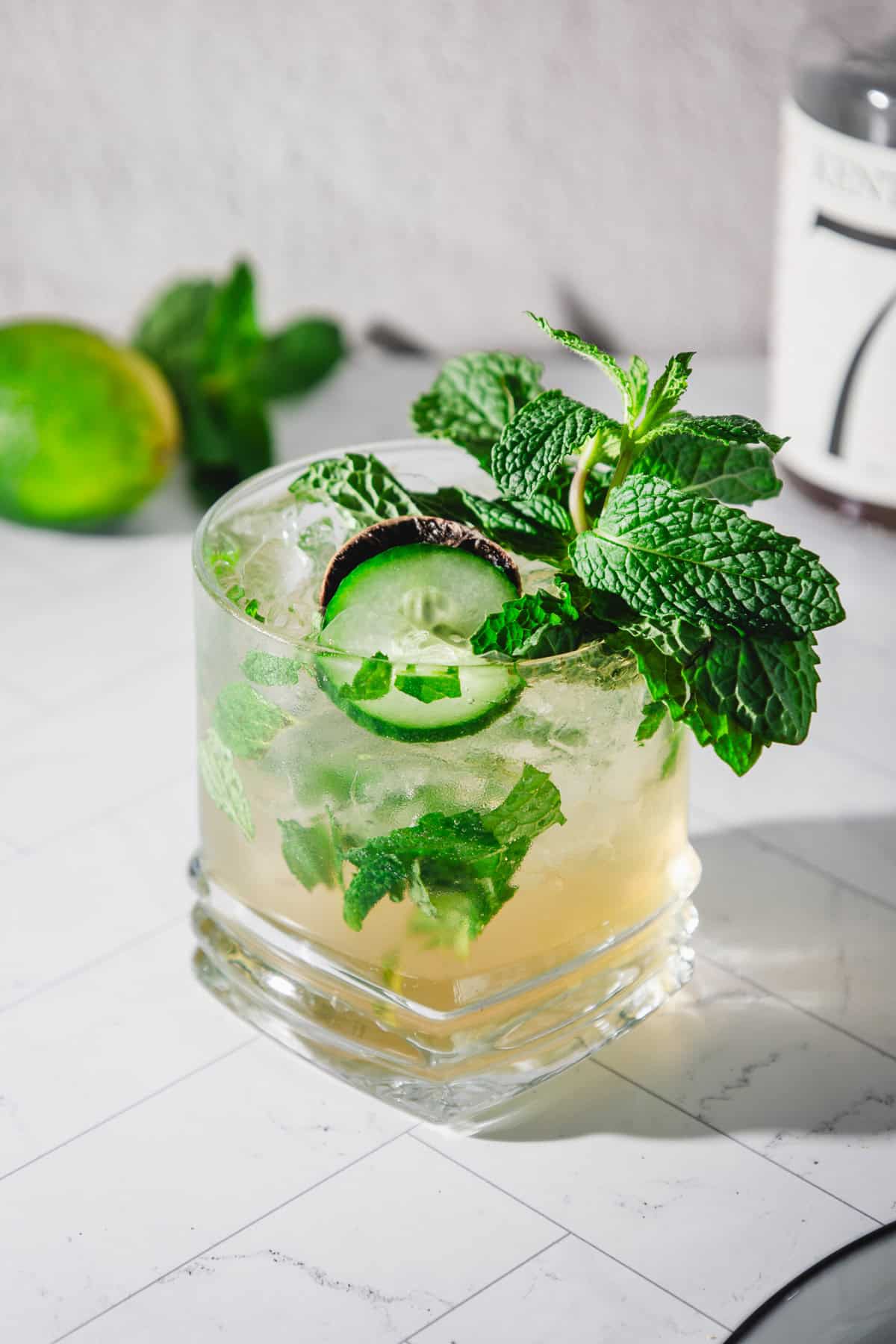 A virgin mint julep recipe comes to life in this cocktail, garnished with mint leaves and cucumber slices on a white tiled surface.