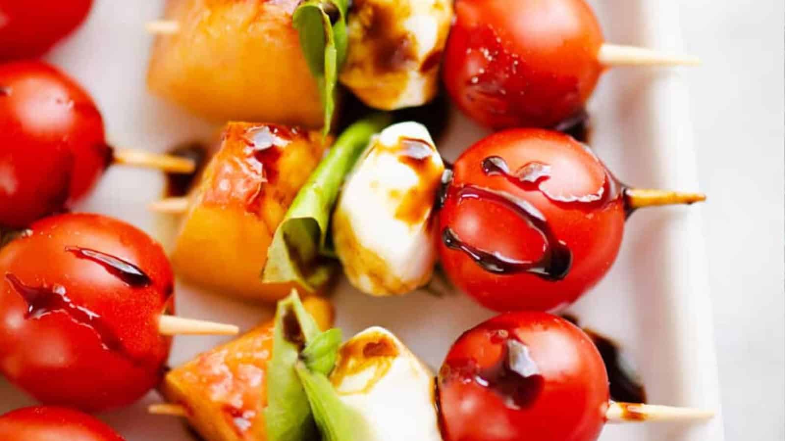 Caprese skewers with tomatoes, mozzarella, basil, and glaze on a white plate.