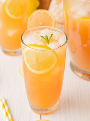 Lemonade Iced Tea with lemon slices and mint served in two glasses and a pitcher on a white table with a wooden board.