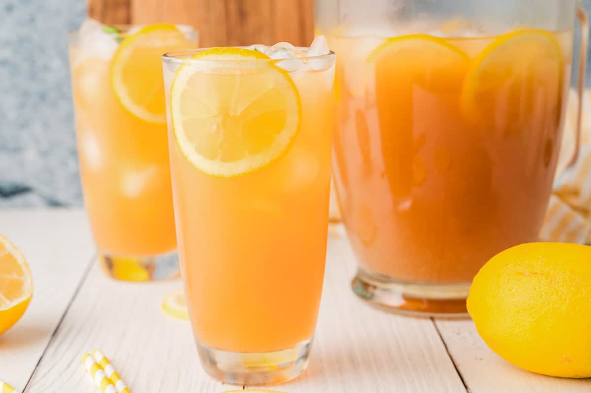 Lemonade Iced Tea with lemon slices served in glasses and a pitcher, set on a white table with fresh lemons nearby.