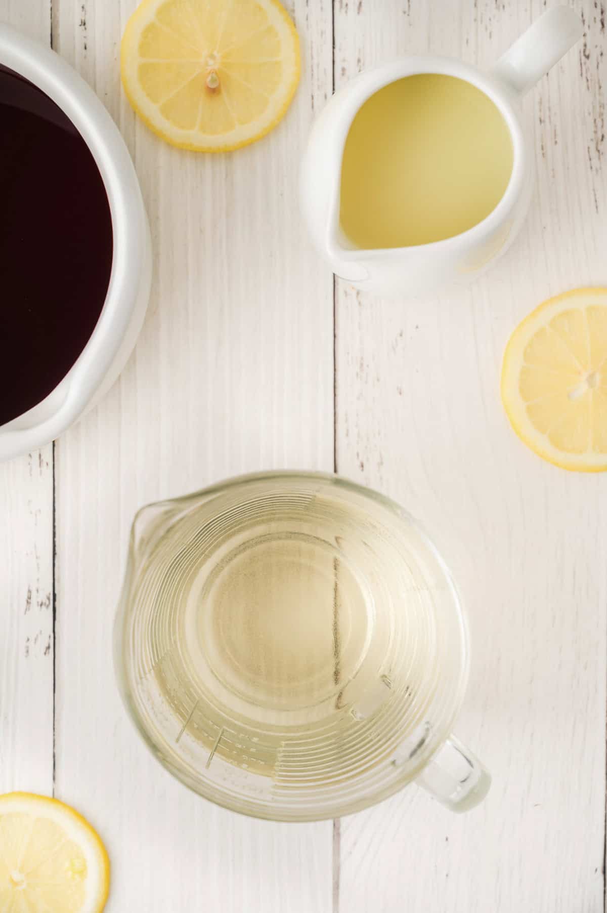 Top view of a glass measuring cup, lemon slices, red liquid in a bowl, and yellow liquid in a small pitcher—perfect ingredients for crafting refreshing Lemonade Iced Tea at home.
