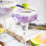 Purple lavender margarita mocktail served in a sugar-rimmed glass, garnished with lime and lavender, with lime slices nearby.