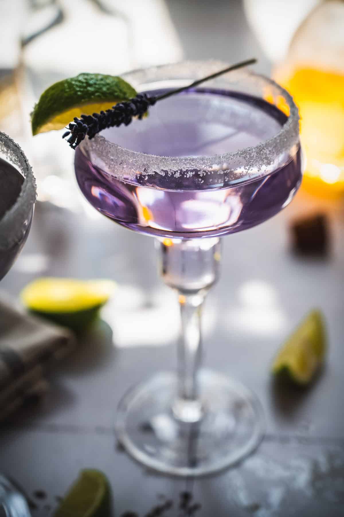 A purple lavender margarita mocktail in a sugar-rimmed glass, garnished with lime and a sprig of lavender.