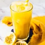 A tall glass of iced passion fruit juice with a striped straw sits next to fresh passion fruit halves, showcasing the refreshing allure of this vibrant fruit juice.