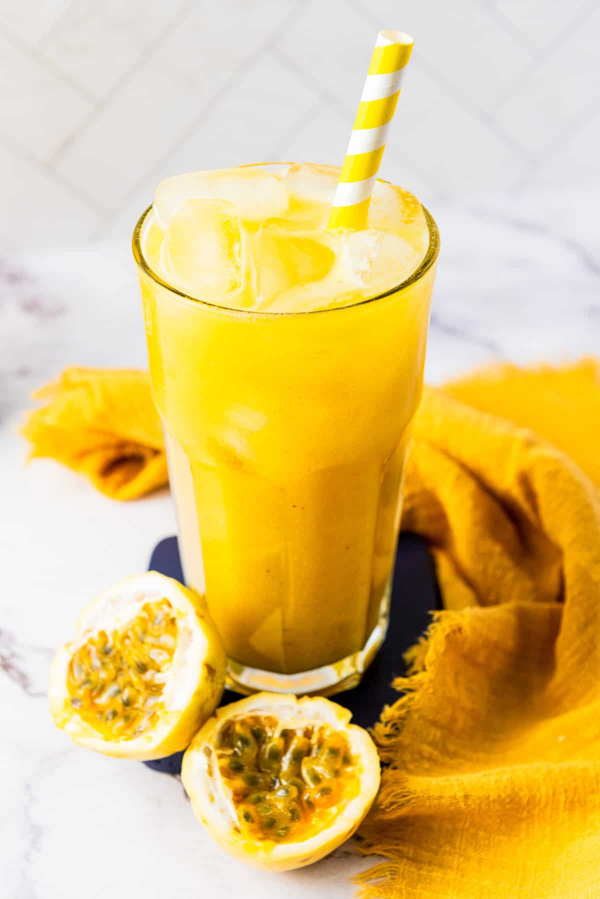 A tall glass of iced passion fruit juice with a striped straw sits next to fresh passion fruit halves, showcasing the refreshing allure of this vibrant fruit juice.