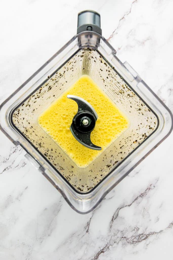 Top view of a blender filled with vibrant yellow passion fruit juice on a white marble surface.