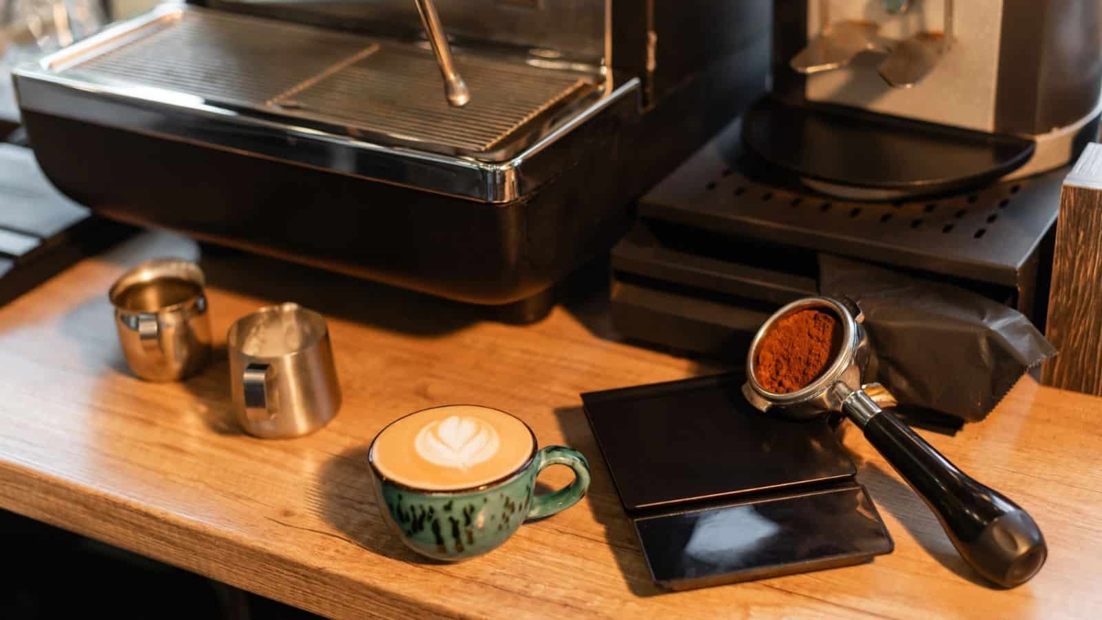 A cup of latte with latte art, coffee grounds, and an espresso machine on a wooden counter—perfect inspiration for your home café or to spark new coffee bar ideas.