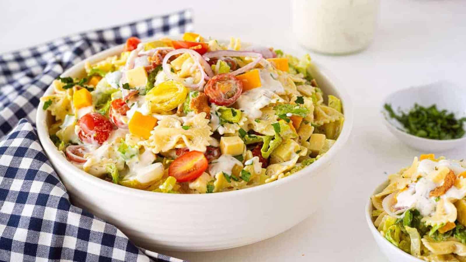 Bowl of salad with pasta, tomatoes, cheese, greens, and dressing on a checkered napkin.