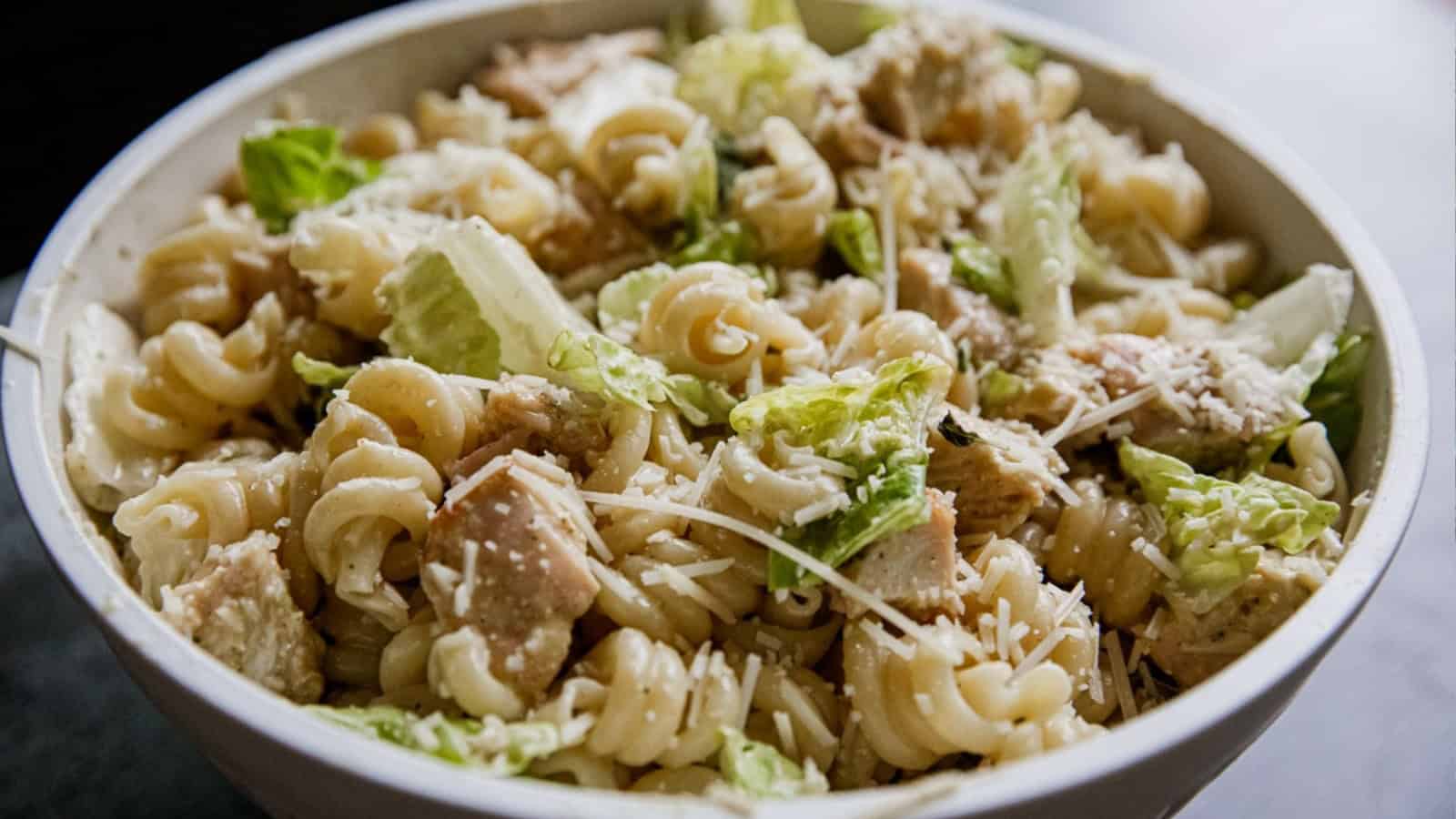 A bowl of pasta salad with lettuce, chicken, croutons, and grated cheese.