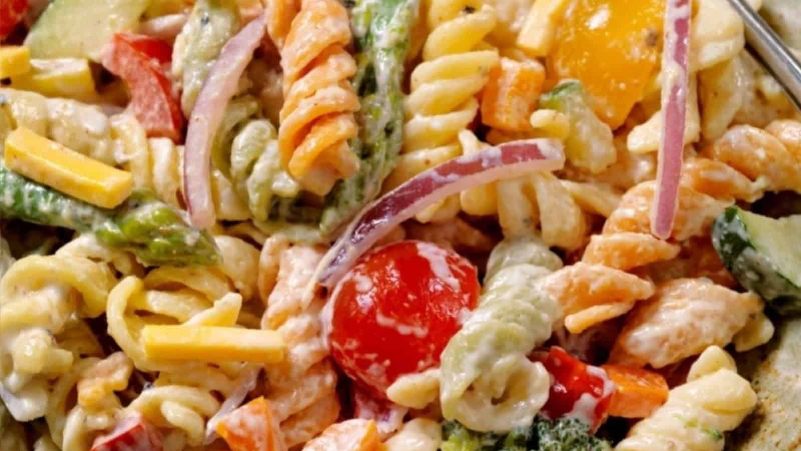 Colorful pasta salad with cherry tomatoes, red onion, cheese, and veggies in a creamy dressing.