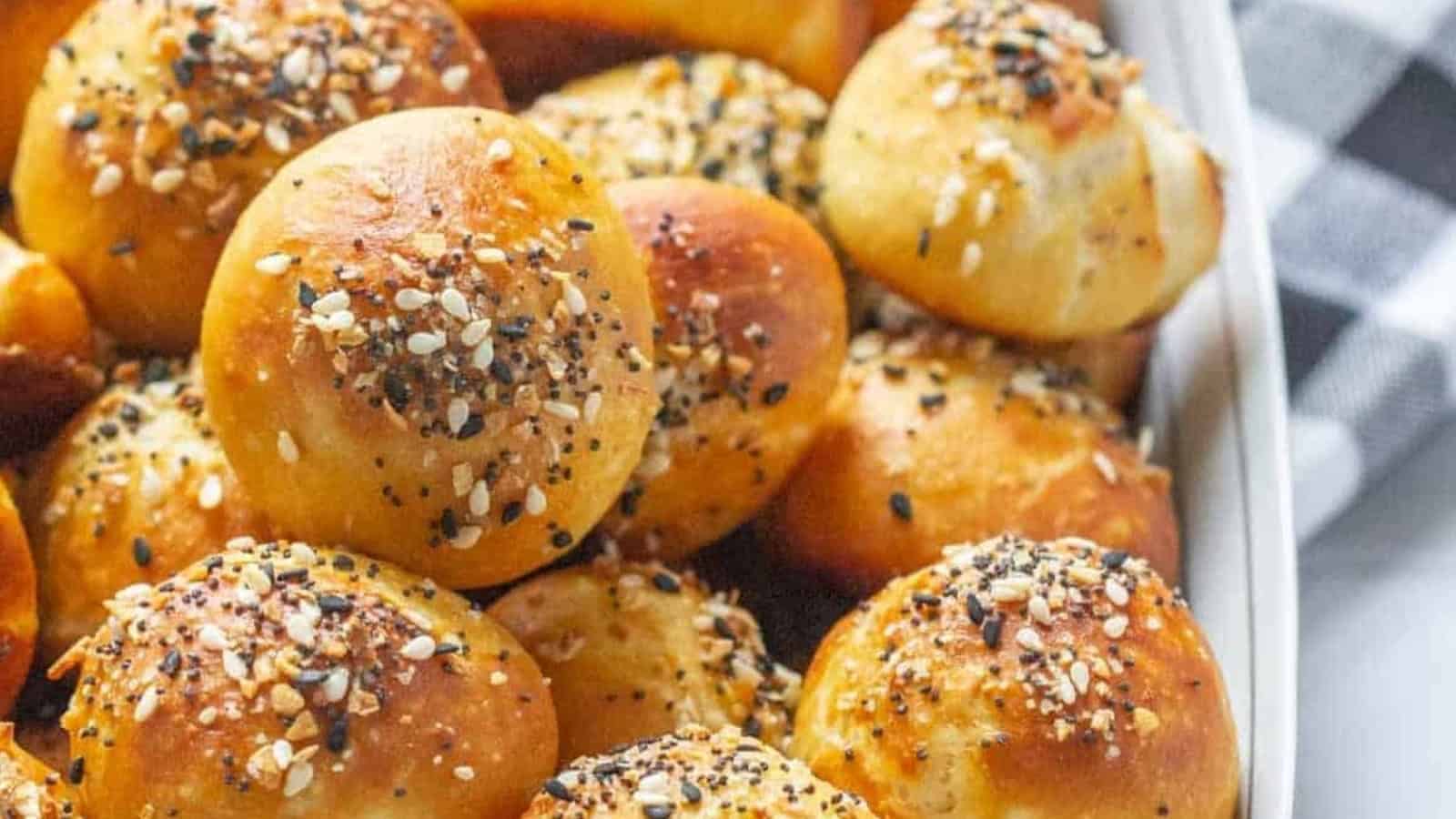Golden-brown bread rolls topped with mixed seeds and seasoning, arranged closely together in a baking dish.