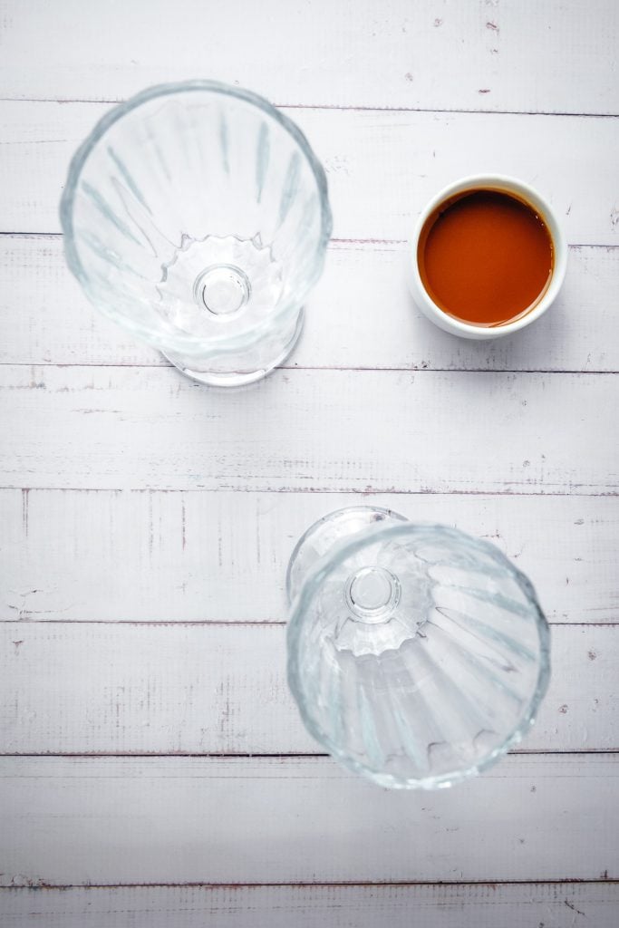 Two empty glass cups and a cup of coffee sit on a white wooden surface, viewed from aboveโperfect for pairing with a creamy Biscoff milkshake or enjoying your favorite sweet treat.