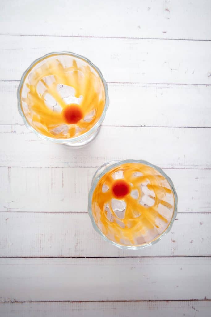 Two empty dessert glasses with caramel and a red spot on the bottom, perfect for serving a creamy Biscoff milkshake, set on a white wooden surface.