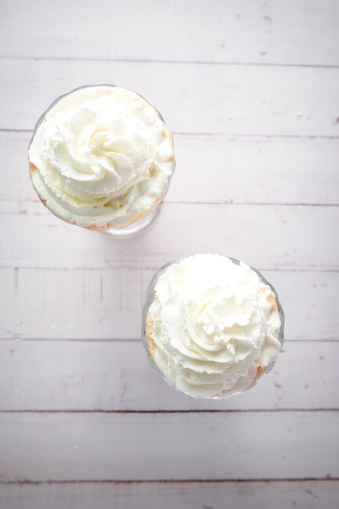 Two glasses of creamy Biscoff milkshake topped with whipped cream, viewed from above on a white wooden surface.