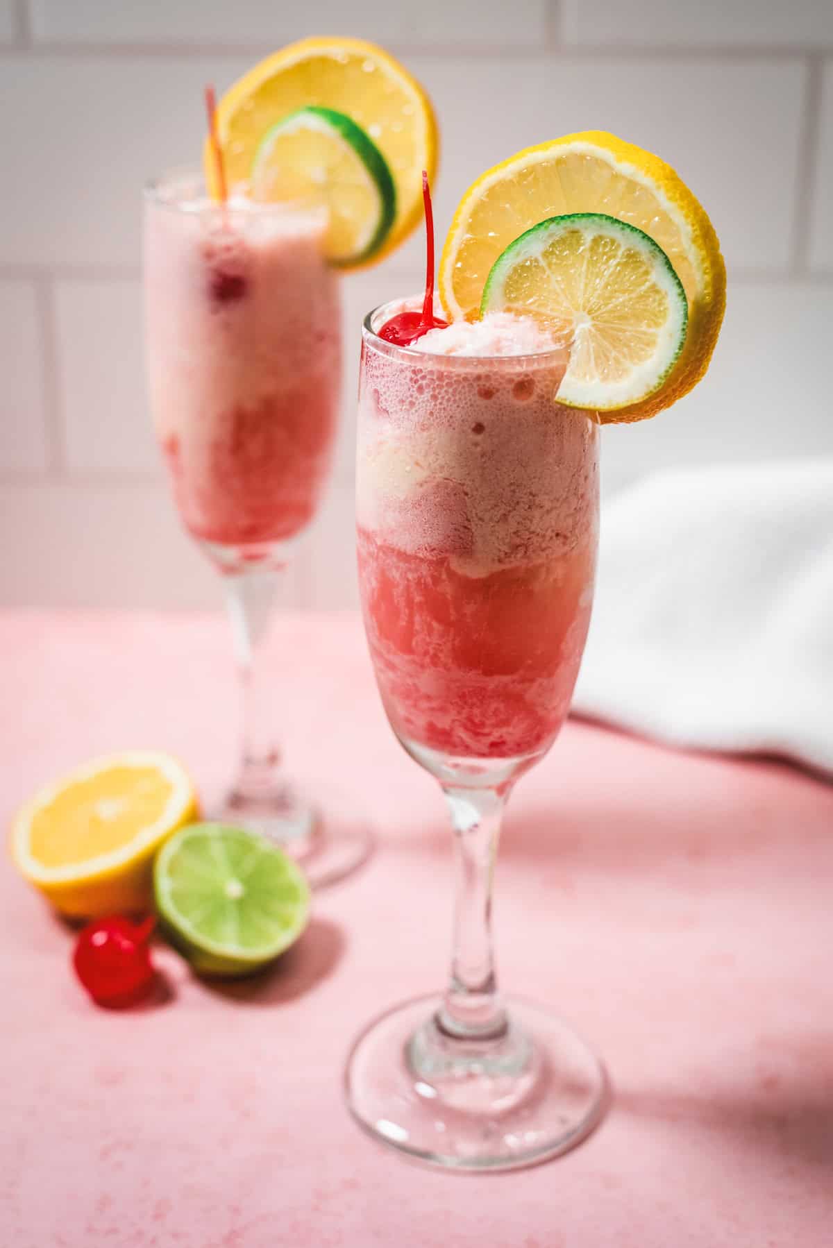 Two fruity Shirley Temple Floats in champagne glasses, garnished with orange, lemon, lime slices, and cherries.